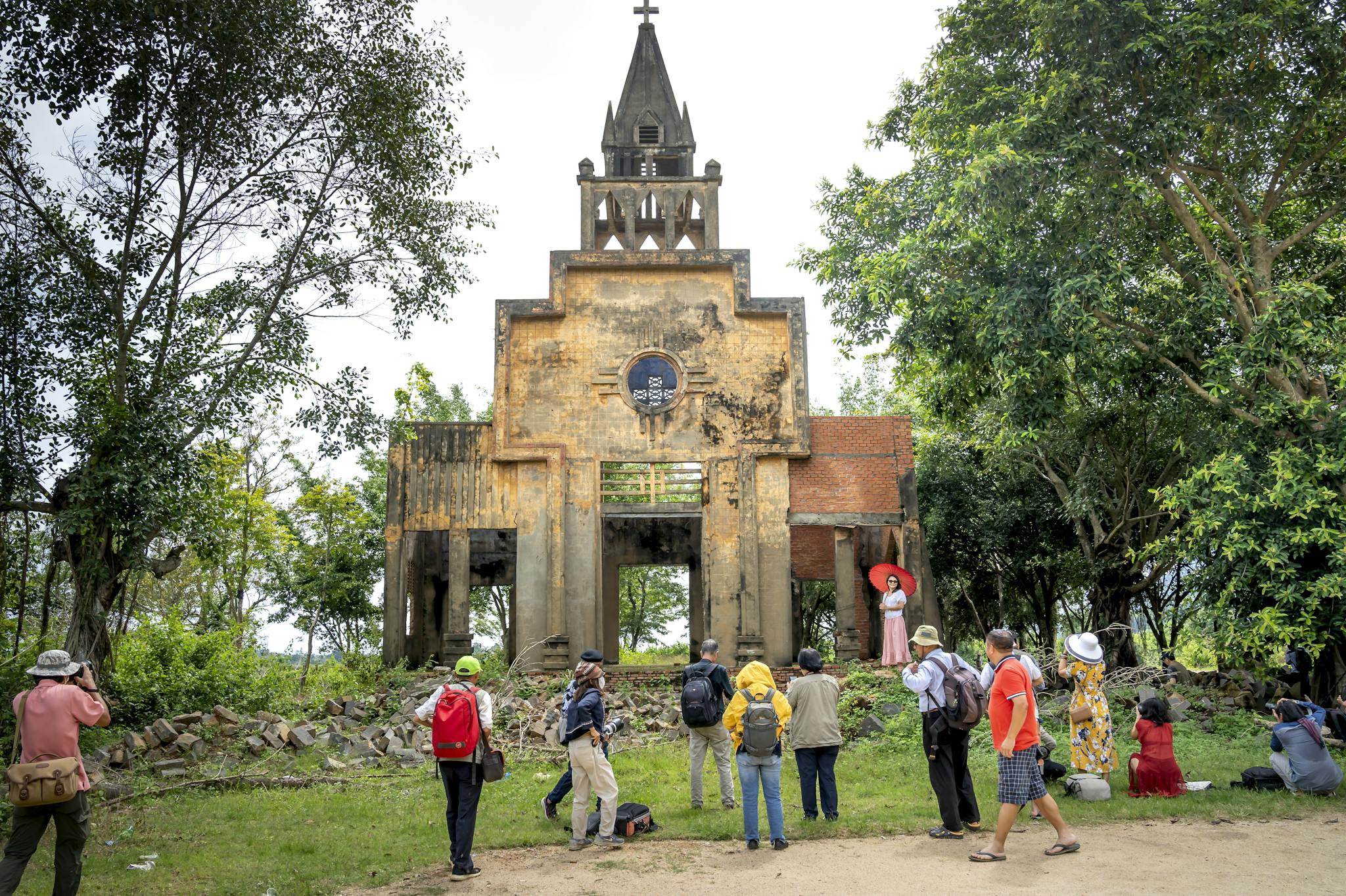 A group of tourists visits a historic, abandoned church ruin surrounded by lush greenery.
