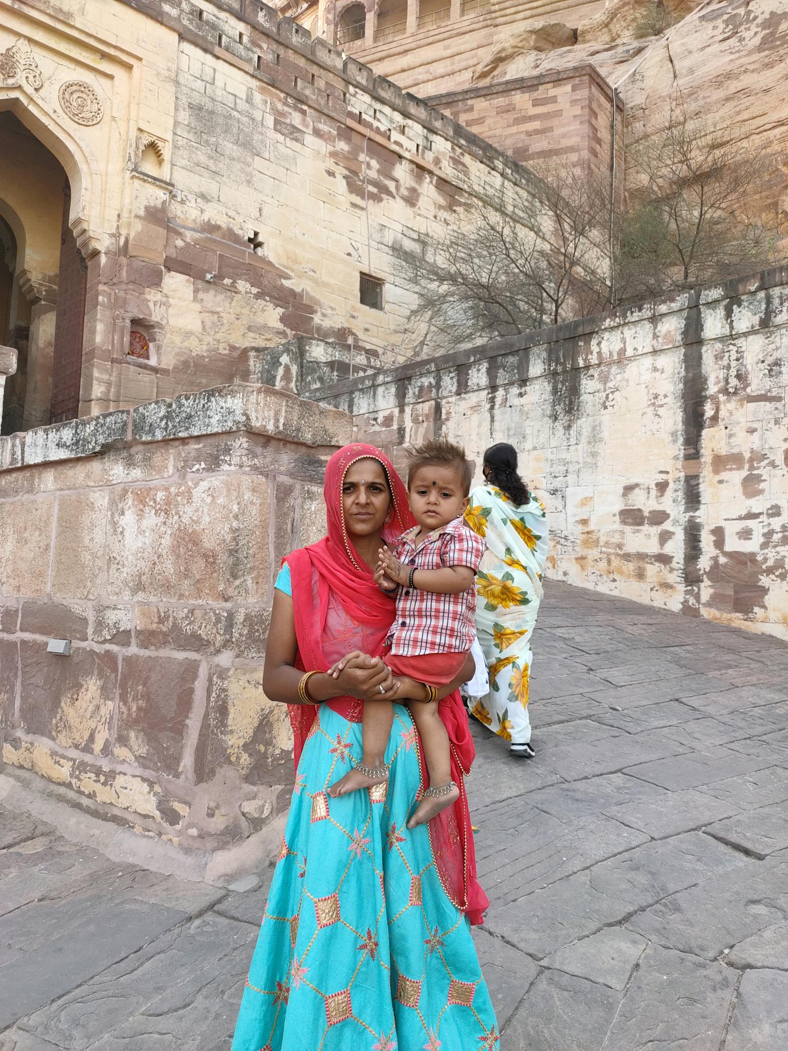 A mother and son in vibrant traditional Indian clothing at a historic site.